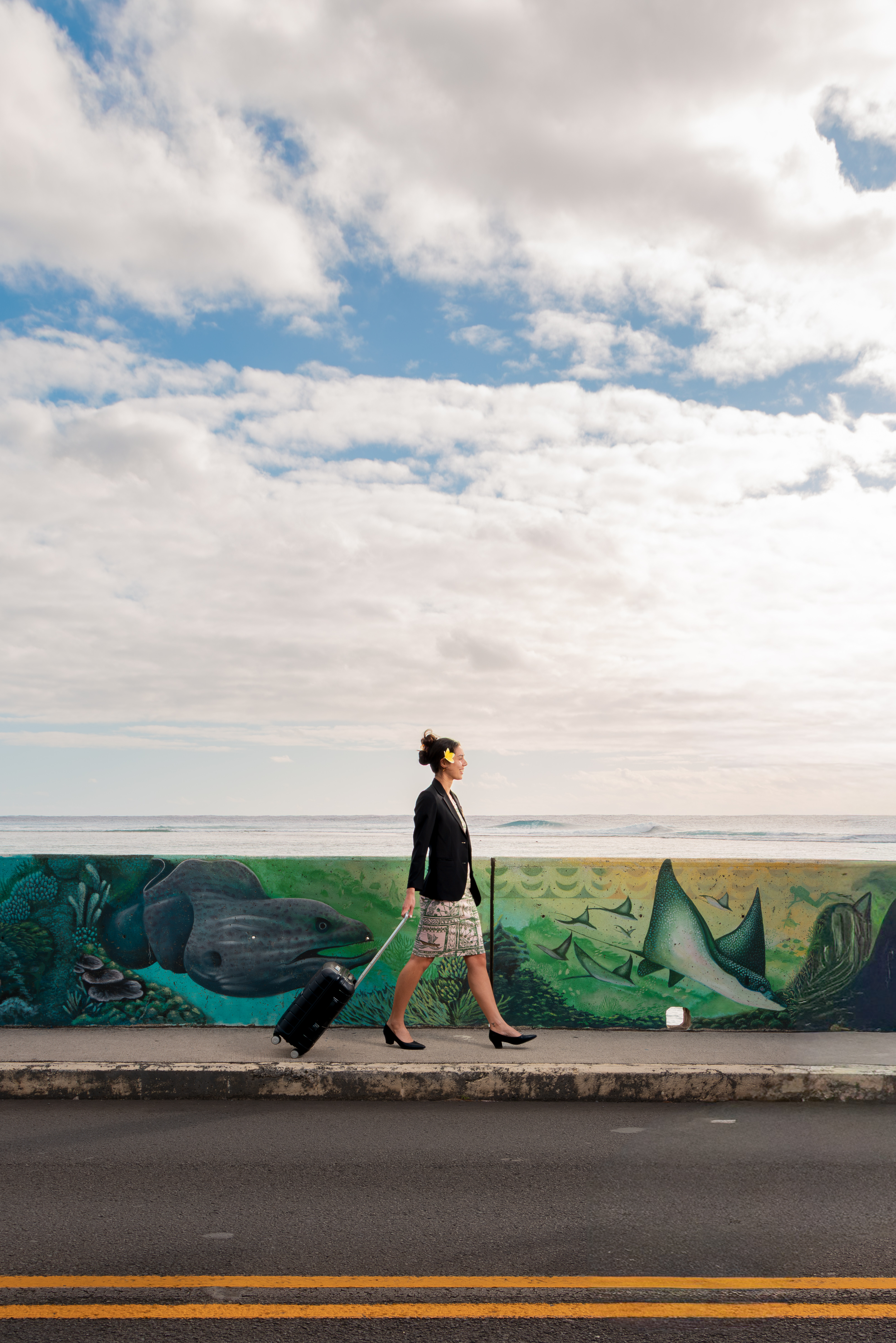 A traveller pulling a suitcase beside a sea-wall mural.